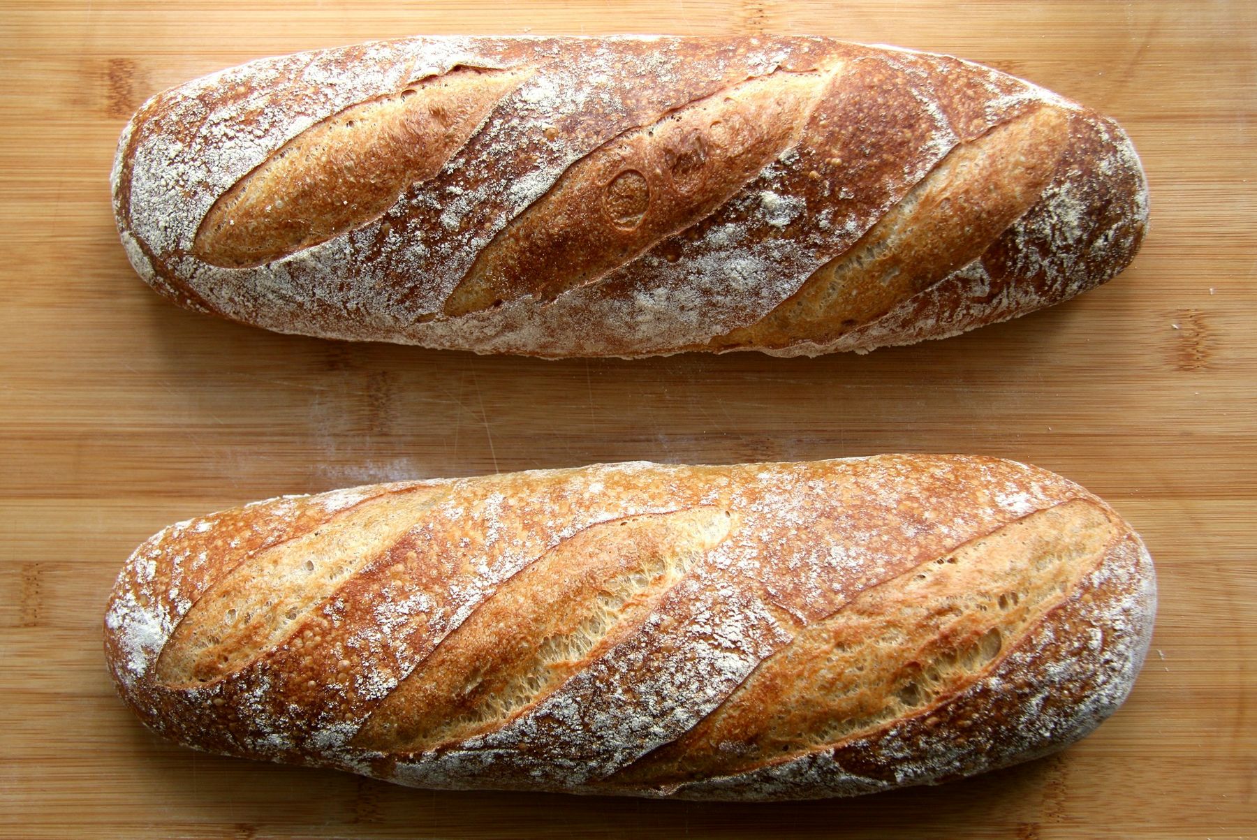 Deux baguettes de tradition dorées, grignes ouvertes, sur un plan de travail en bois.