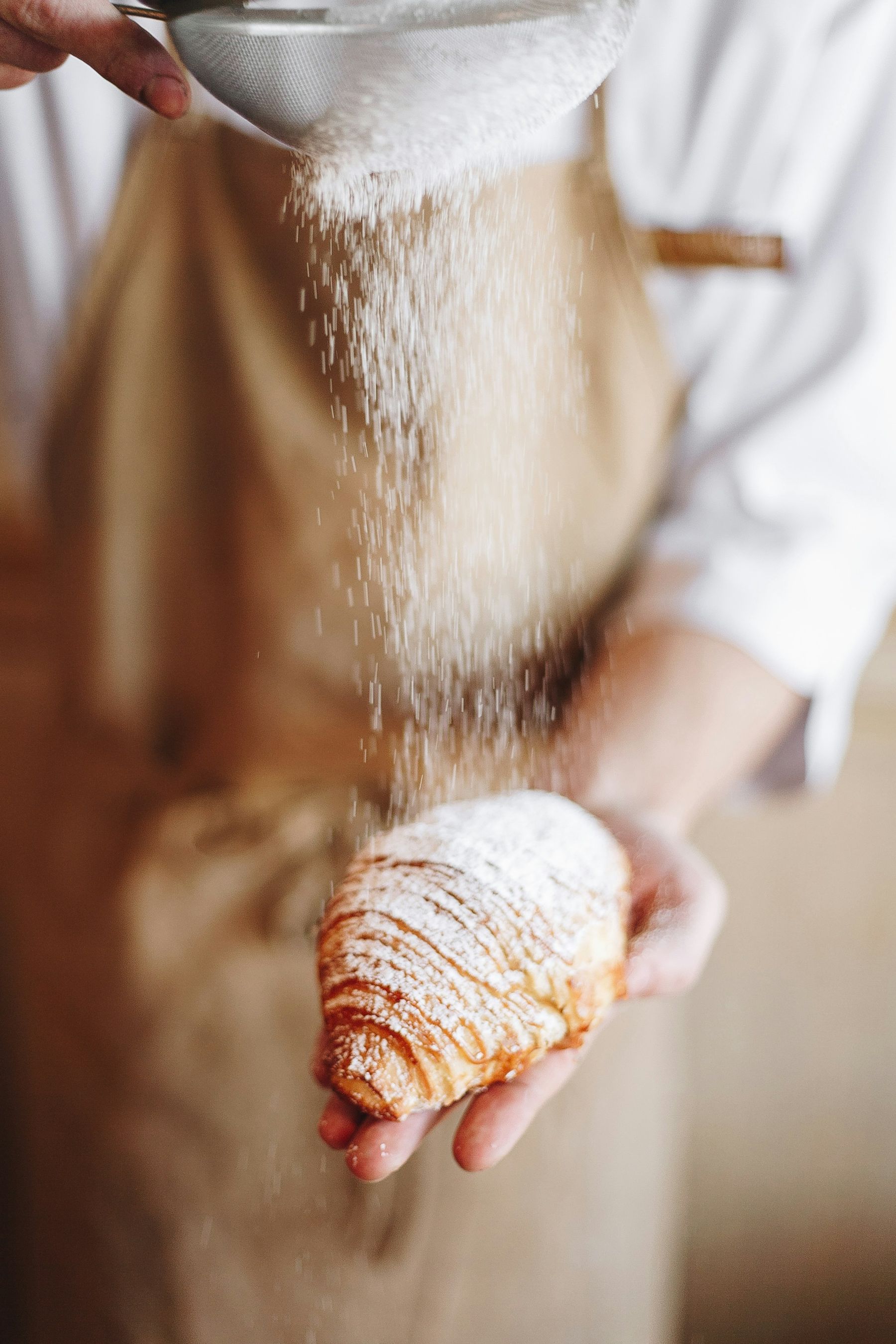 Du sucre glace tamisé sur une viennoiserie tenue dans la main.