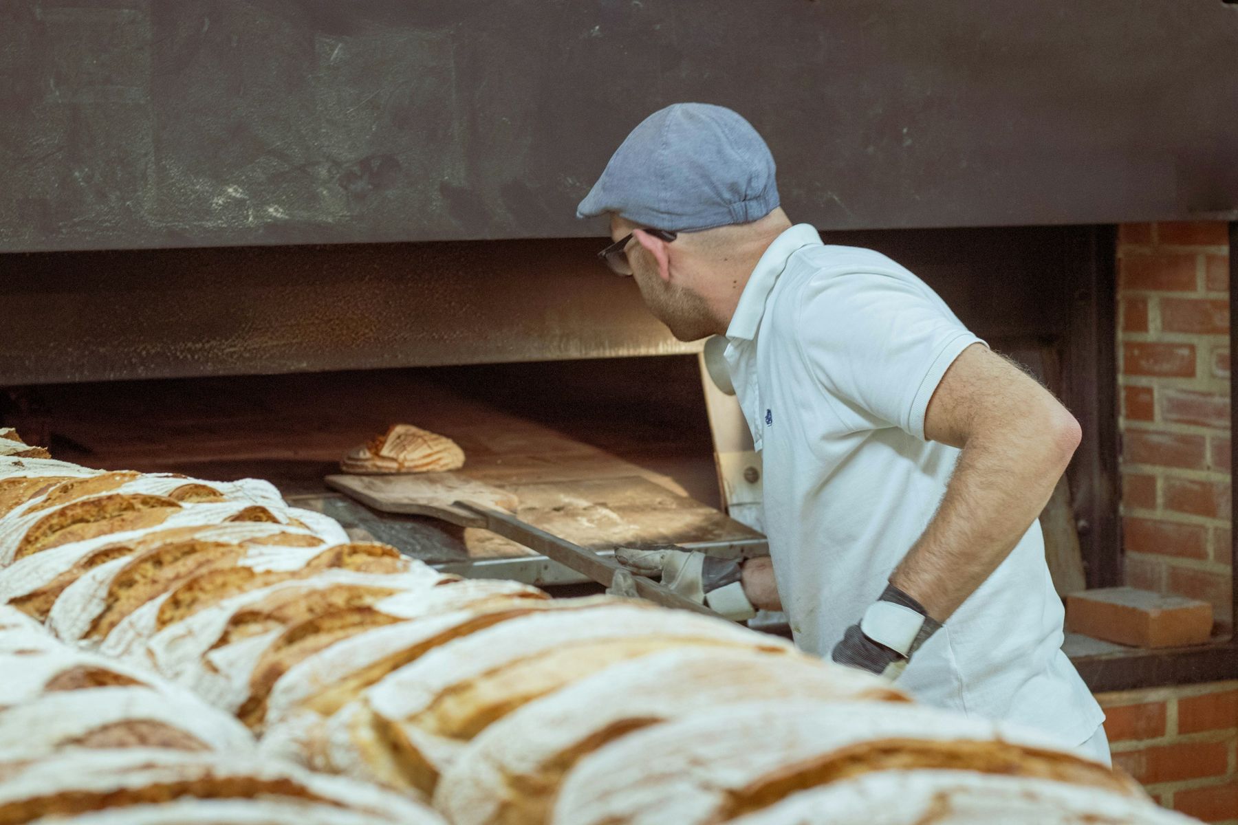 Au fournil, un boulanger enfourne les miches dans le four à bois en briques.