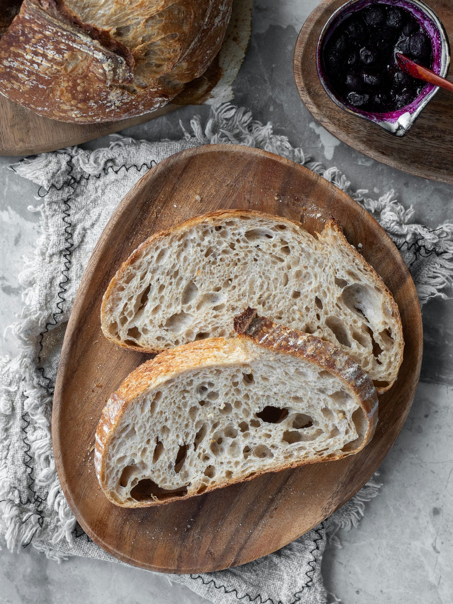 Deux tranches de miche au levain, la mie alvéolée, sur une planche en bois.